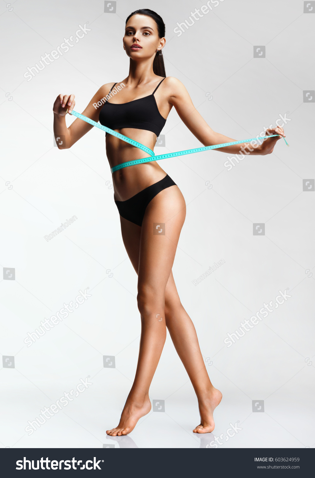 Slim girl in black underwear with a measuring ribbon at the waist. Photo of beautiful  brunette girl with perfect body. Fitness or body care concept #603624959