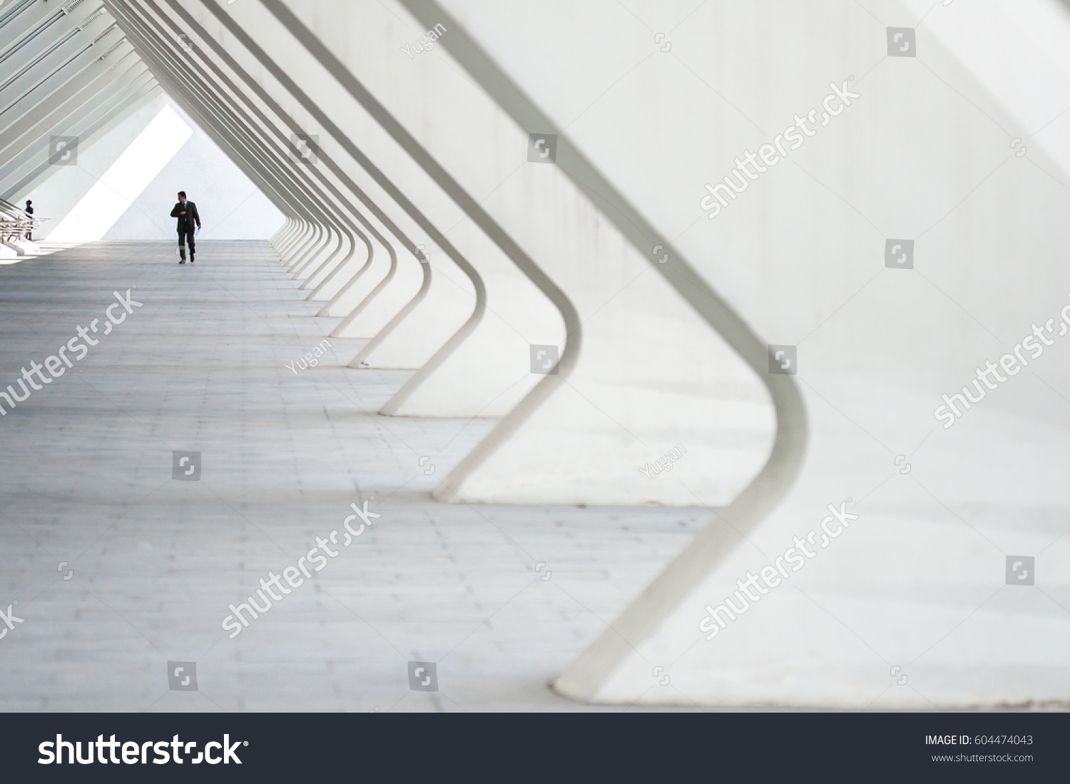 People in the architectural perspective. The sloping lines of the architecture. The man in the suit comes in a bright corridor in a modern building #604474043