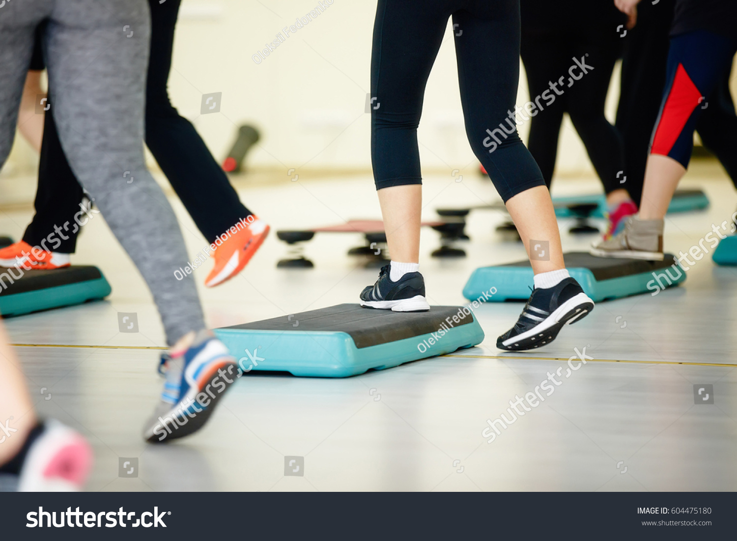 Women doing aerobic class with steppers to people group on fitness center detail of raised feet during aerobic step exercise at gym aerobics and people concept people working out with steppers in gym. #604475180