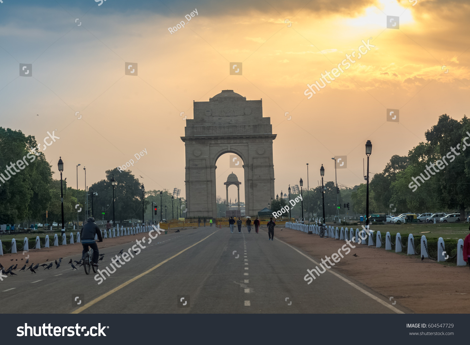 DELHI, INDIA, MARCH 10, 2017: View of Rajpath road New Delhi near India Gate at sunrise with morning walkers enjoying the fresh air. The India Gate, is a war memorial and a notable city landmark. #604547729