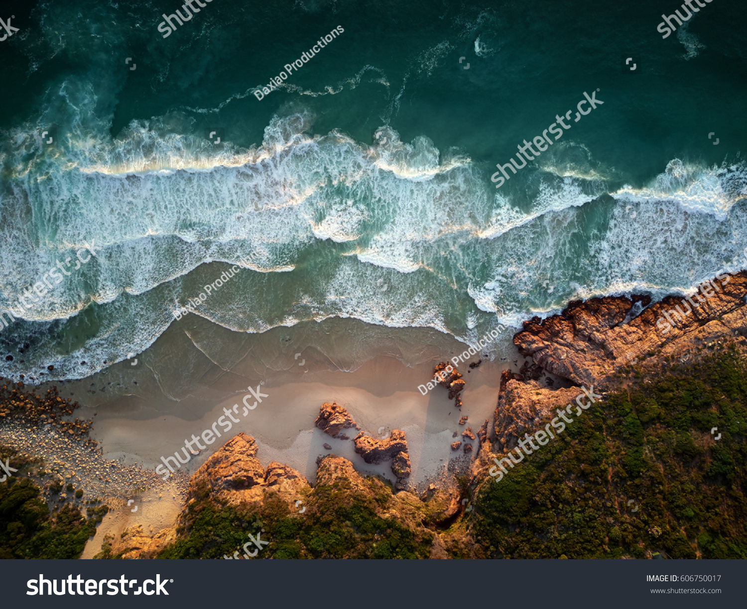 Small waves repeatedly crashing on small sandy shore bay beach with rough rocky coastline, aerial photography overhead #606750017