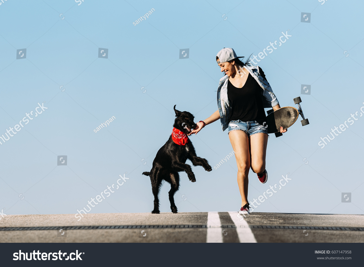 Beautiful young skater playing with her dog in the city. #607147958
