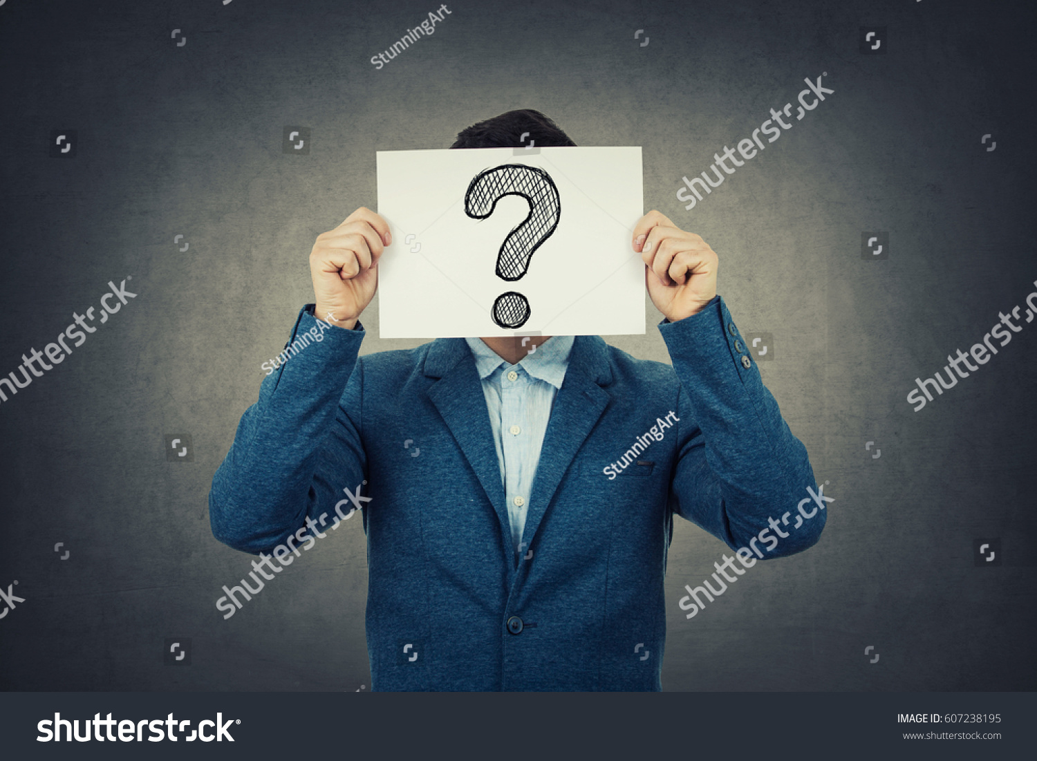 Businessman covering his face using a white paper with drawn question mark, like a mask, for hiding his identity. Isolated gray wall background. #607238195