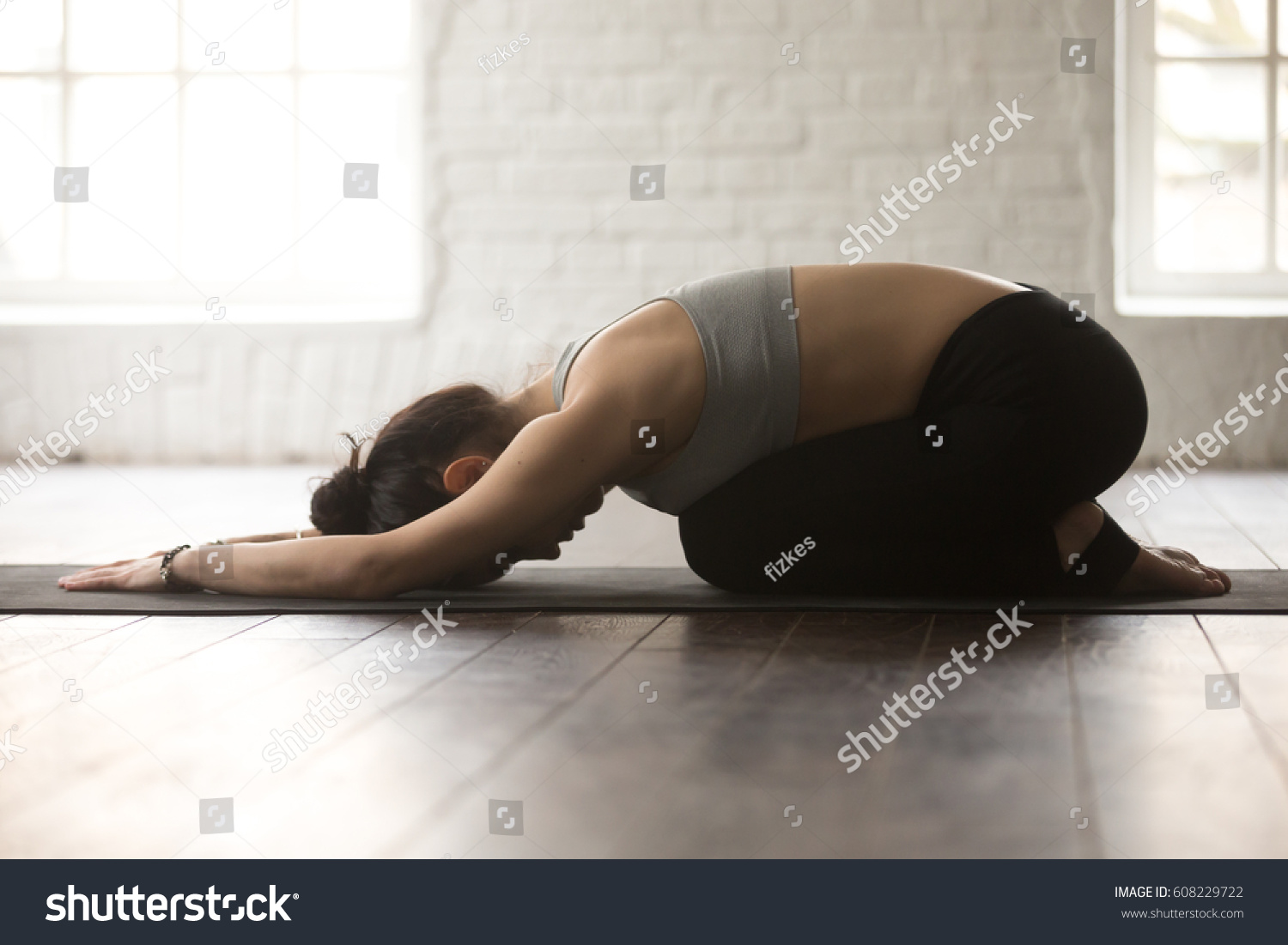 Young attractive sporty yogi woman practicing yoga concept, sitting in Child exercise, Balasana pose, working out, wearing black sportswear, full length, white loft studio background, side view #608229722