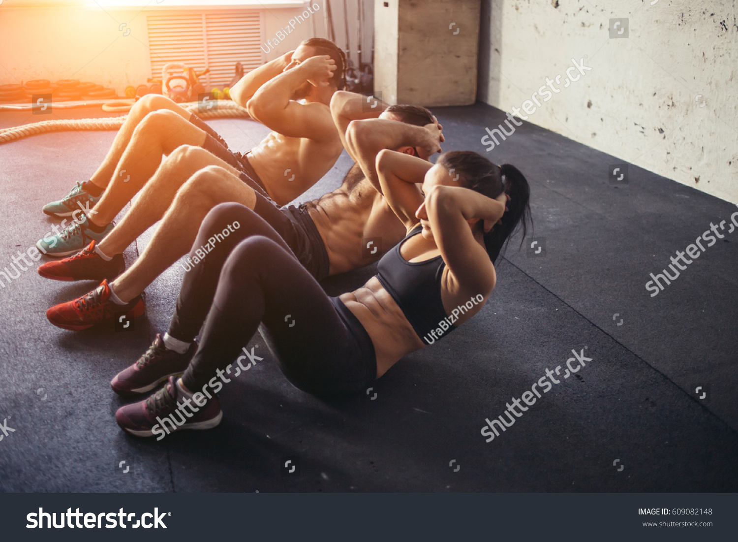 Group of athletic adult men and women performing sit up exercises to strengthen their core abdominal muscles at fitness training #609082148