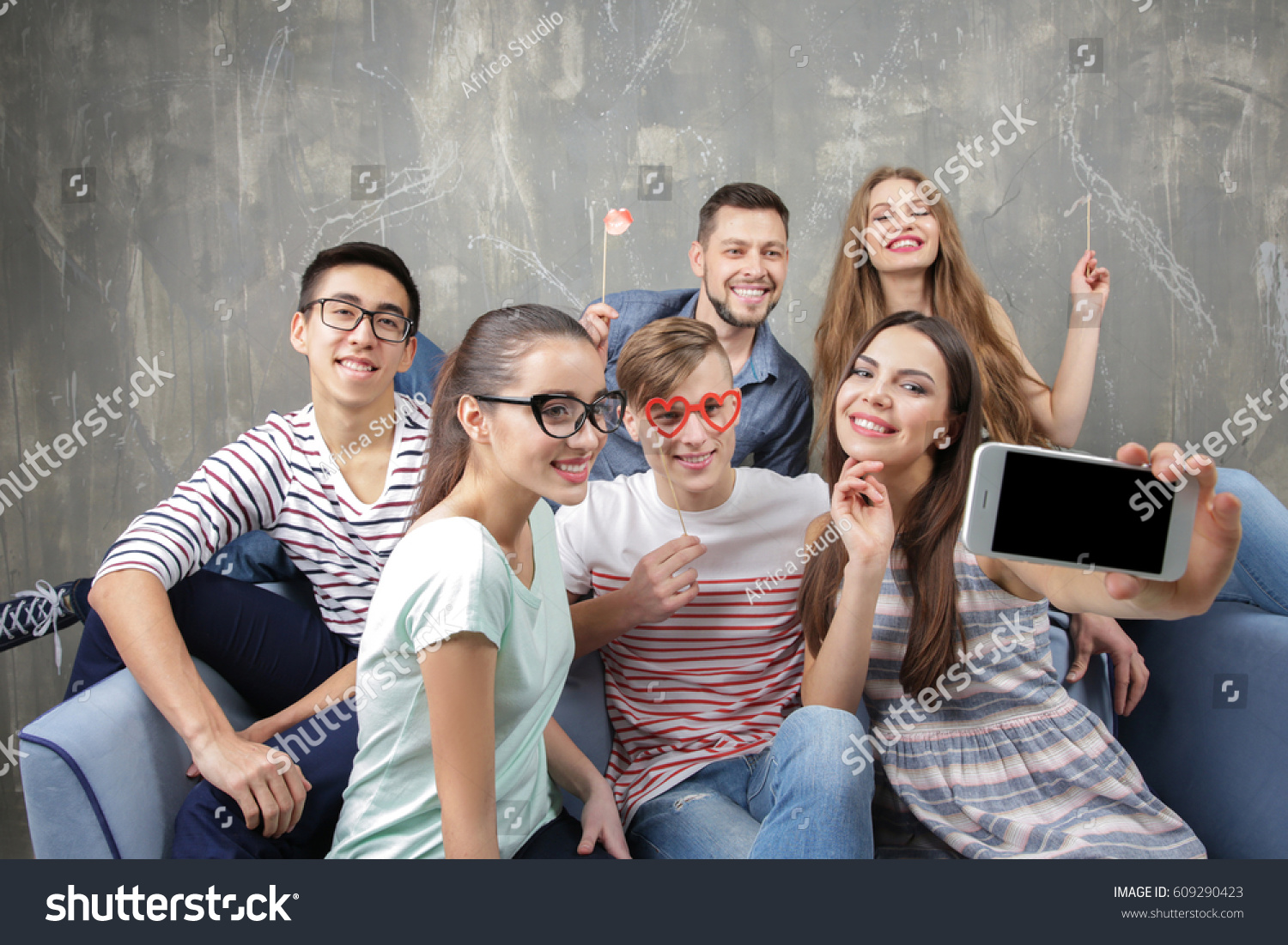 Happy young friends taking selfie while sitting on sofa near grunge wall #609290423