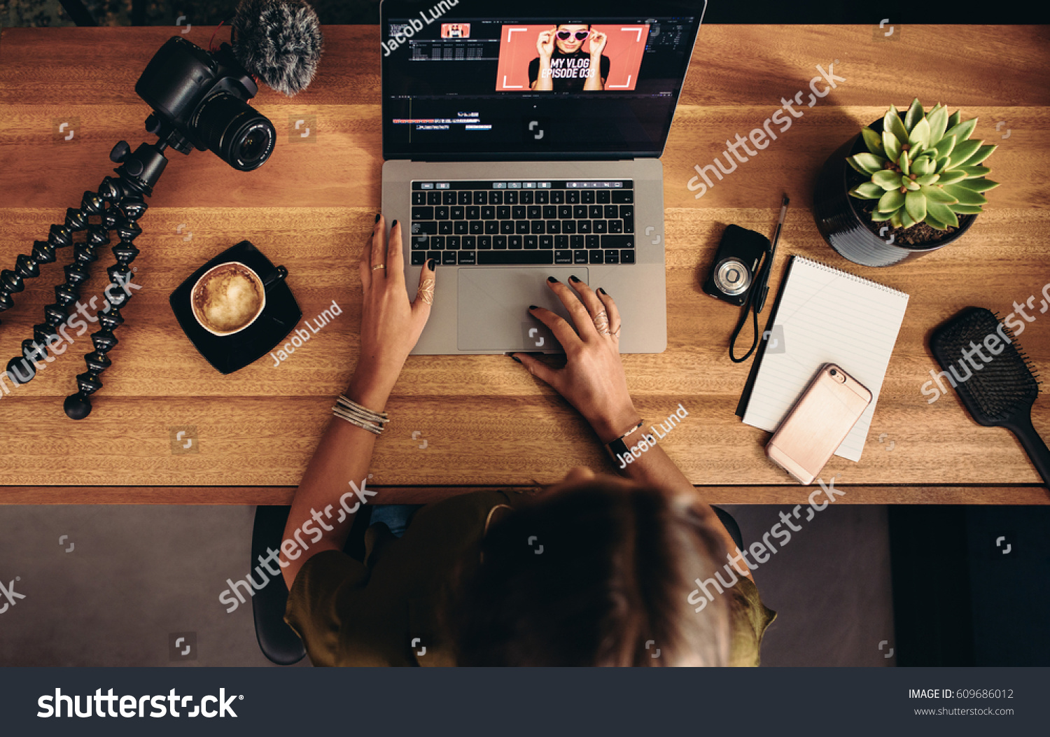 High angle view of female vlogger editing video on laptop. Young woman working on computer with cameras and accessories on table. #609686012