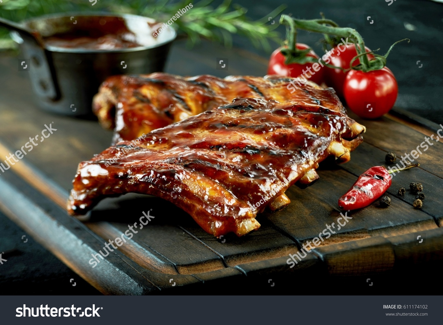 Spicy hot grilled spare ribs from a summer BBQ served with a hot chili pepper and fresh tomatoes on an old vintage wooden cutting board #611174102