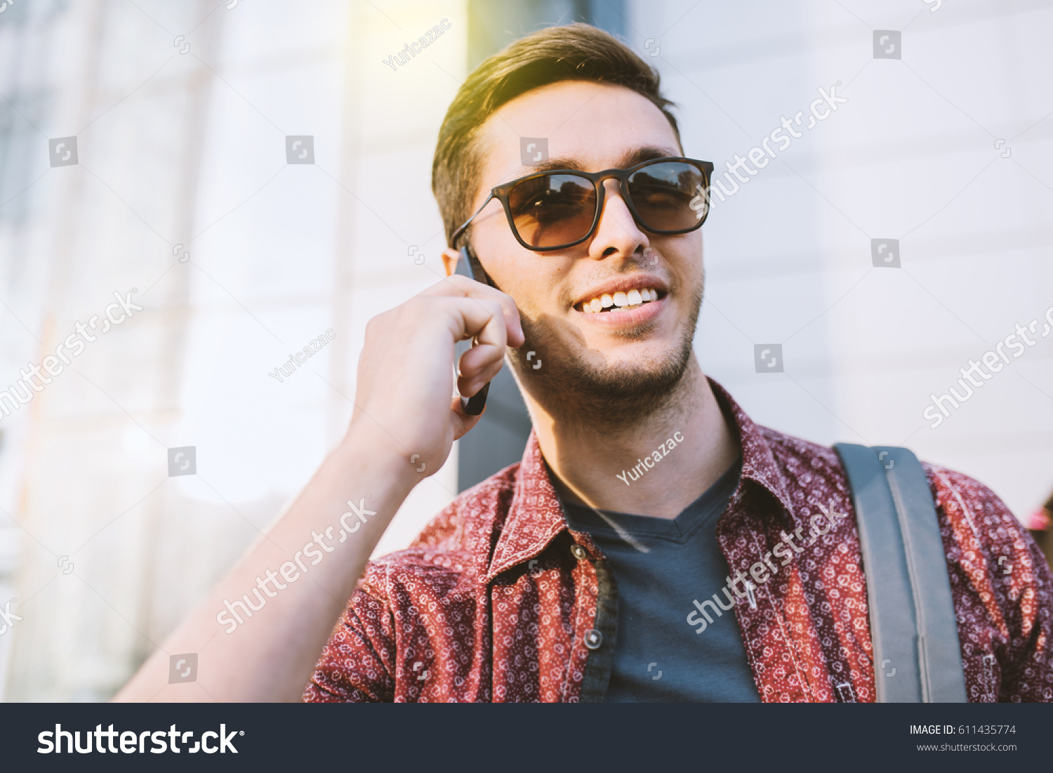 Close up portrait of cheerful attractive smile caucasian man in stylish sunglasses in 
city. Young business man talking on smart phone, on building outdoors. Fashion urban lifestyle concept. Traveler. #611435774