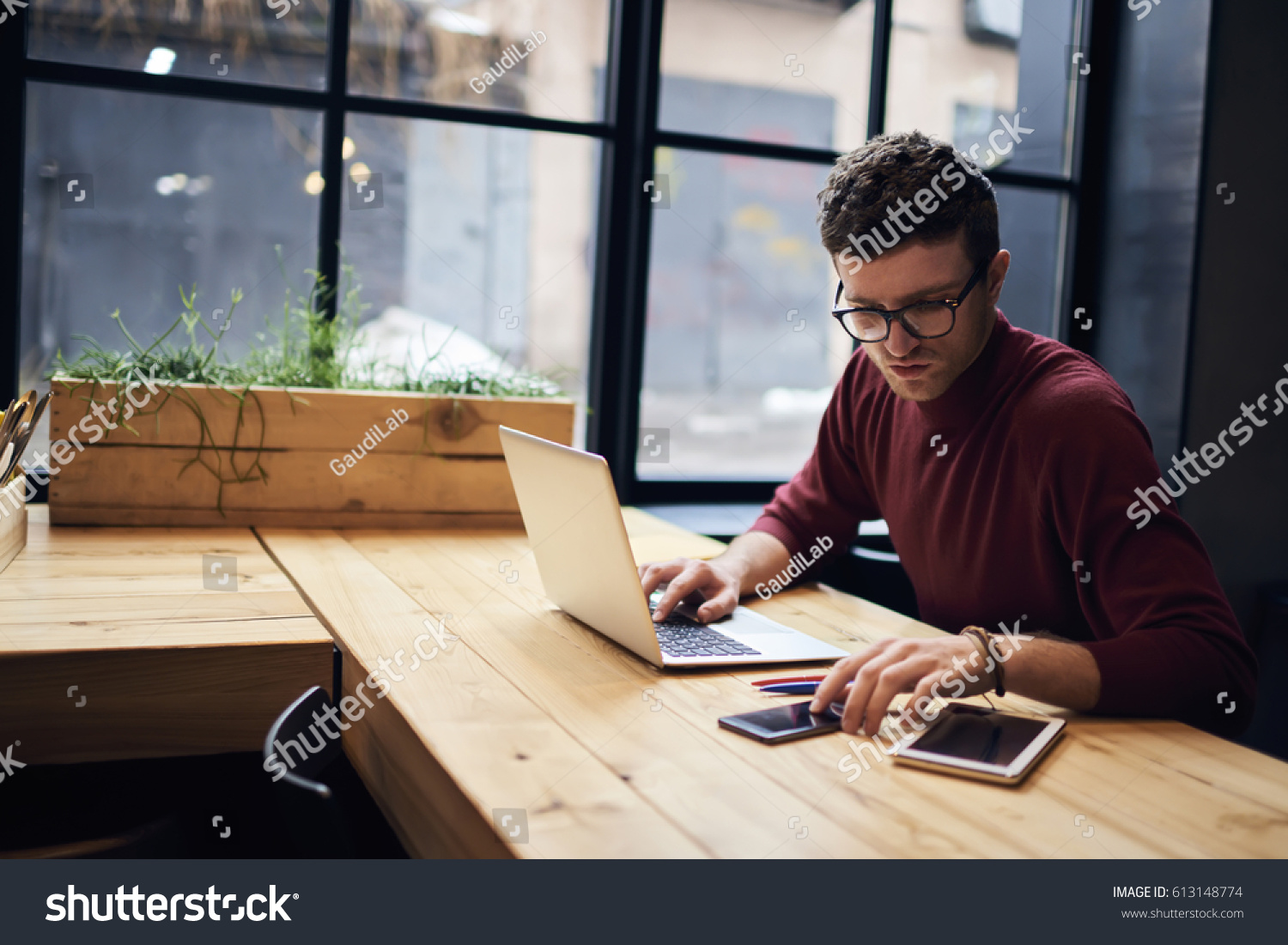 Confident busy male freelancer in trendy eyewear doing remote job using modern technologies checking installation of application on smartphone while surfing net searching information for presentation #613148774
