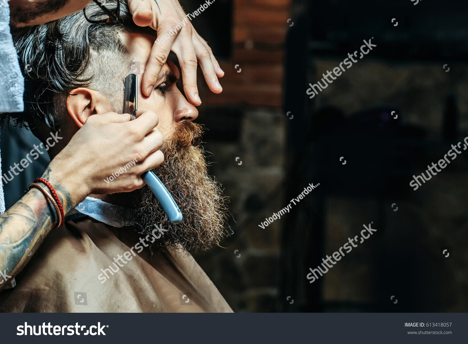 Bearded man with long beard, brutal, caucasian hipster with moustache, getting stylish hair shaving, haircut, with razor by barber or hairdresser with tattoo on hands at barbershop #613418057