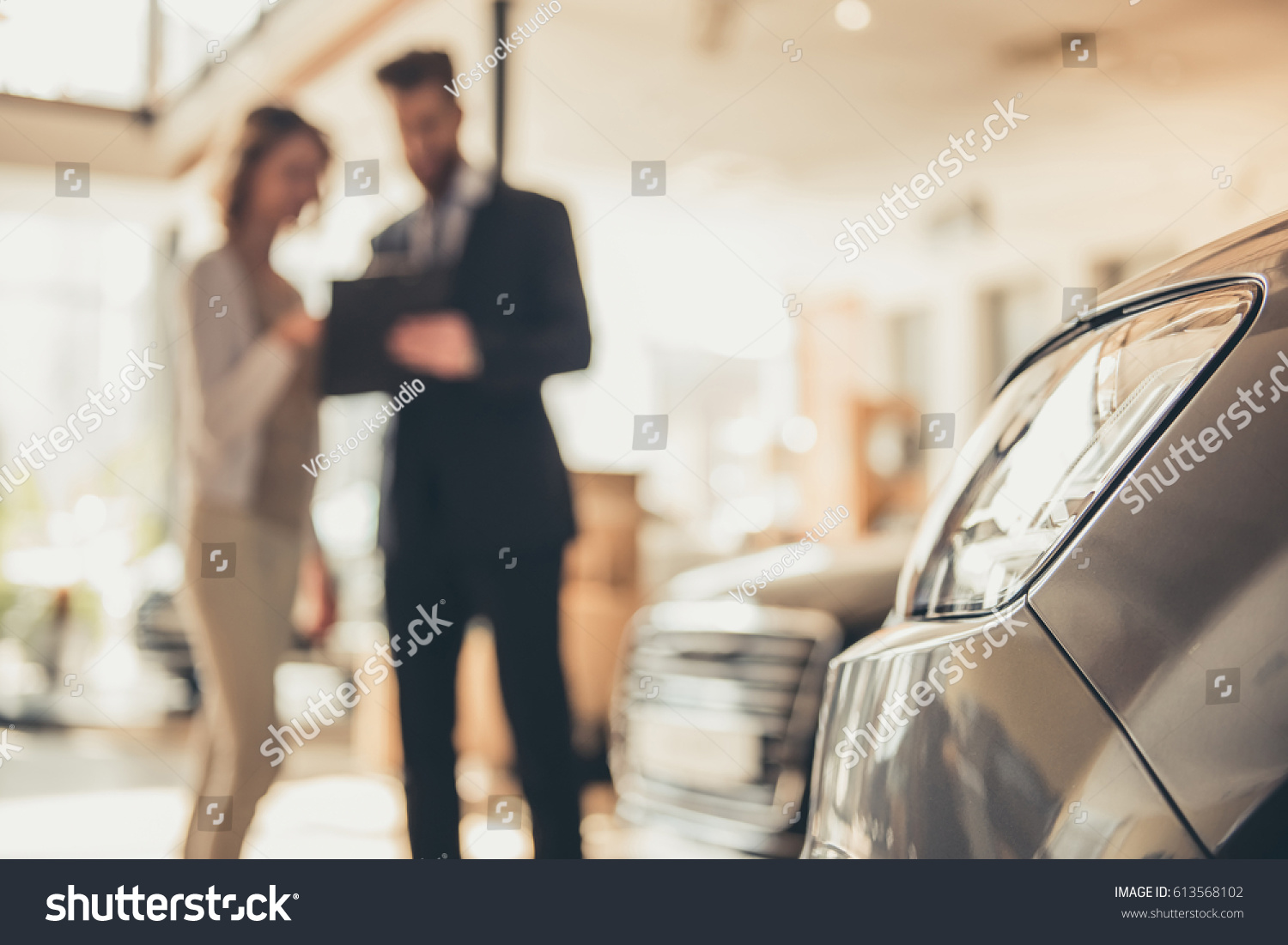 Beautiful young woman is talking to handsome bearded sales manager while choosing a car in dealership #613568102
