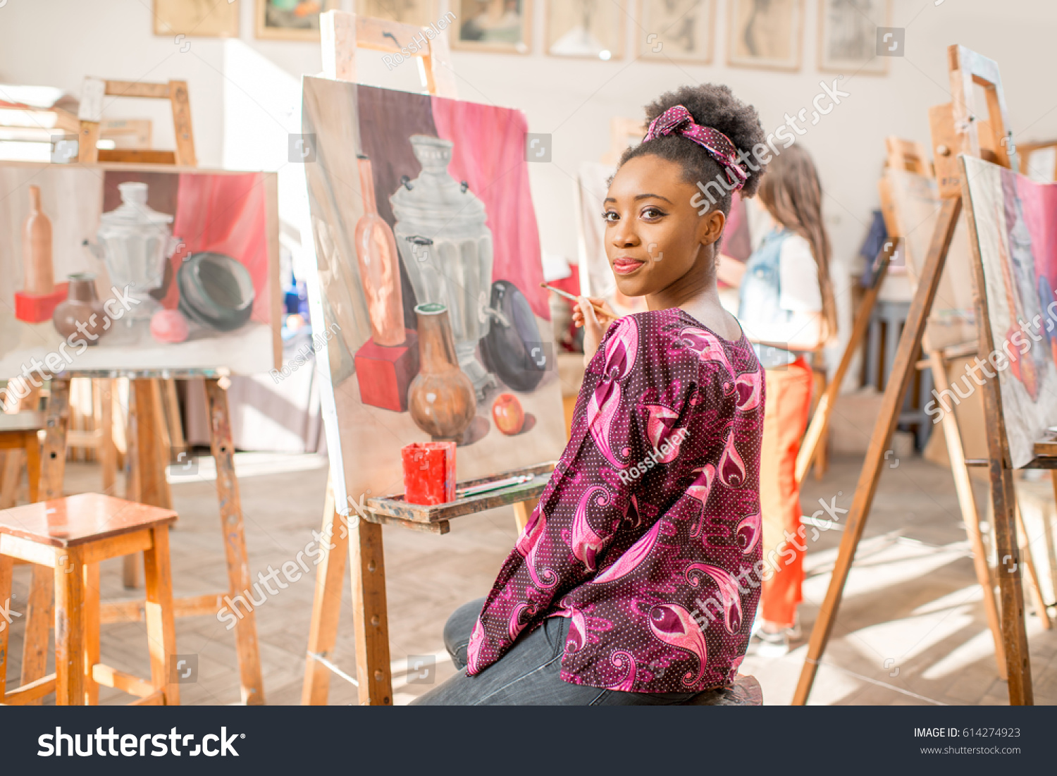 Portrait of a young african student sitting with still life painting at the studio #614274923