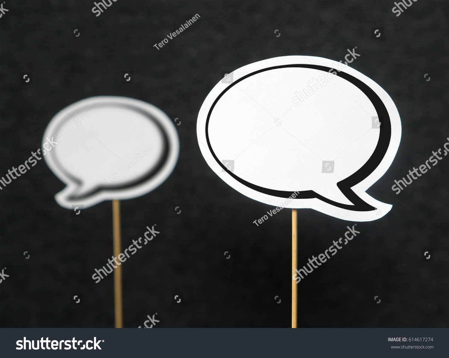 2 blank speech bubbles on a dark black background. The other speech balloon blurred. Chat bubble cut from paper with wooden stick. Discussion, protest and commenting concept with copy space for text. #614617274