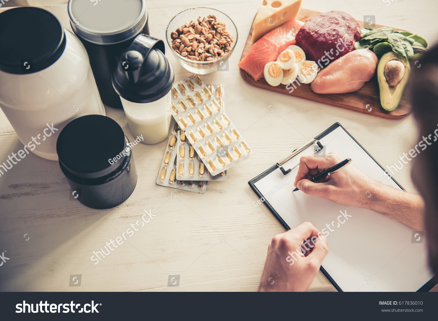 Cropped image of handsome young sportsman making notes while preparing sport nutrition in kitchen at home #617836010
