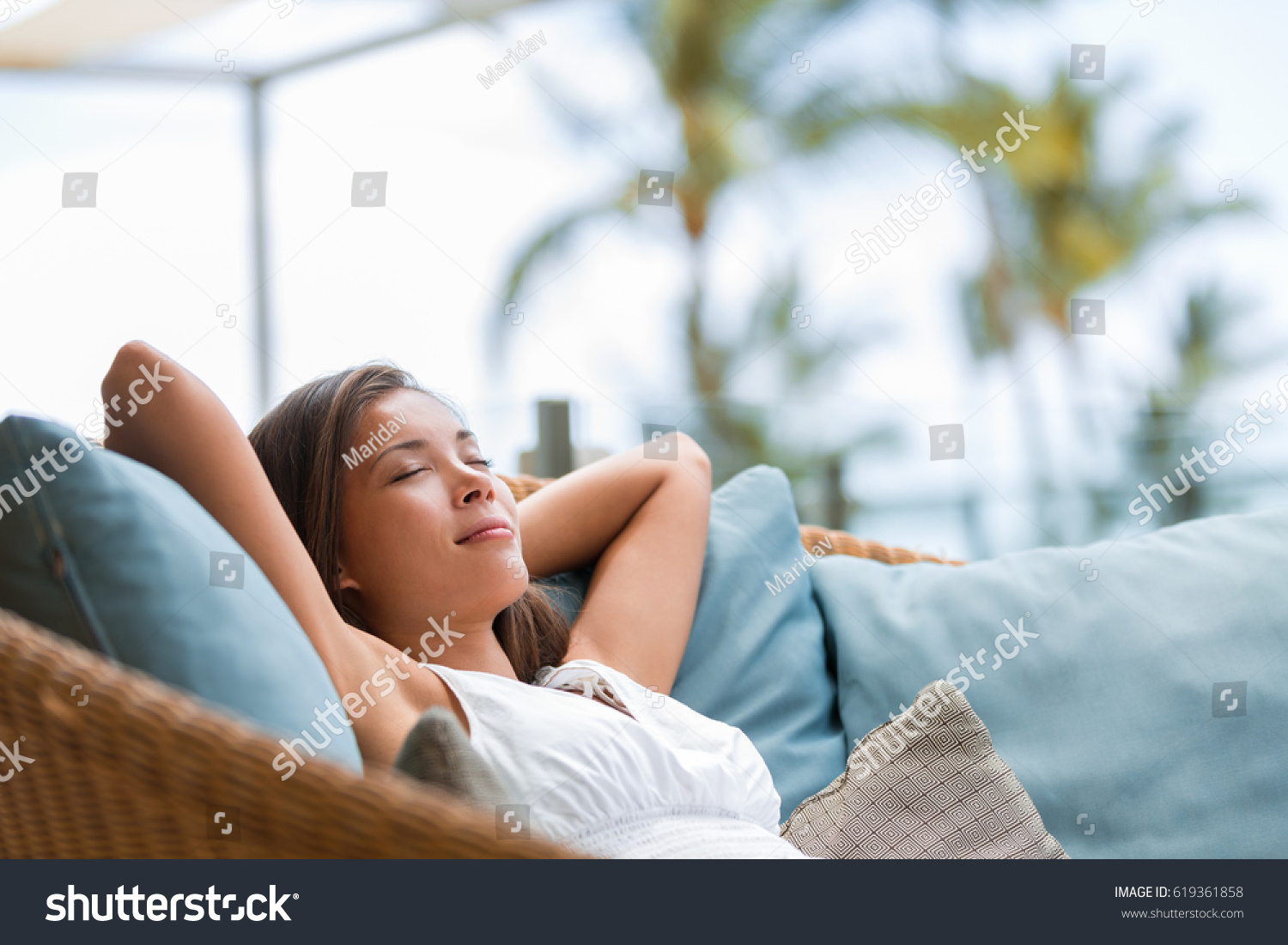 Home lifestyle woman relaxing sleeping on sofa on outdoor patio living room. Happy lady lying down on comfortable pillows taking a nap for wellness and health. Tropical vacation. #619361858