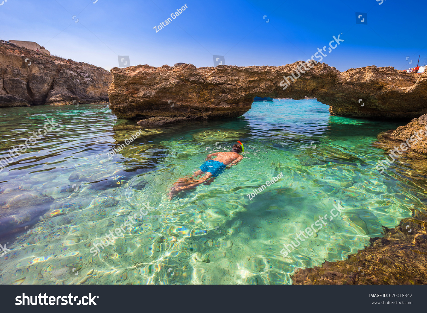 Blue Lagoon, Malta - Snorkeling tourist at the caves of the Blue Lagoon on the island of Comino on a bright sunny summer day with blue sky #620018342