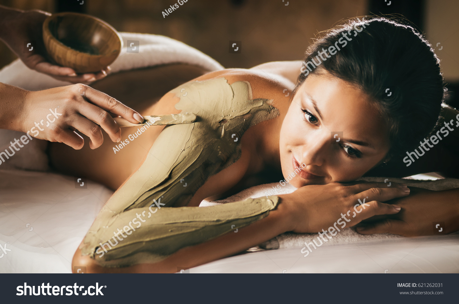 The girl enjoys mud body mask in a spa salon. Focus on the hand with the stick. Luxury treatment. #621262031