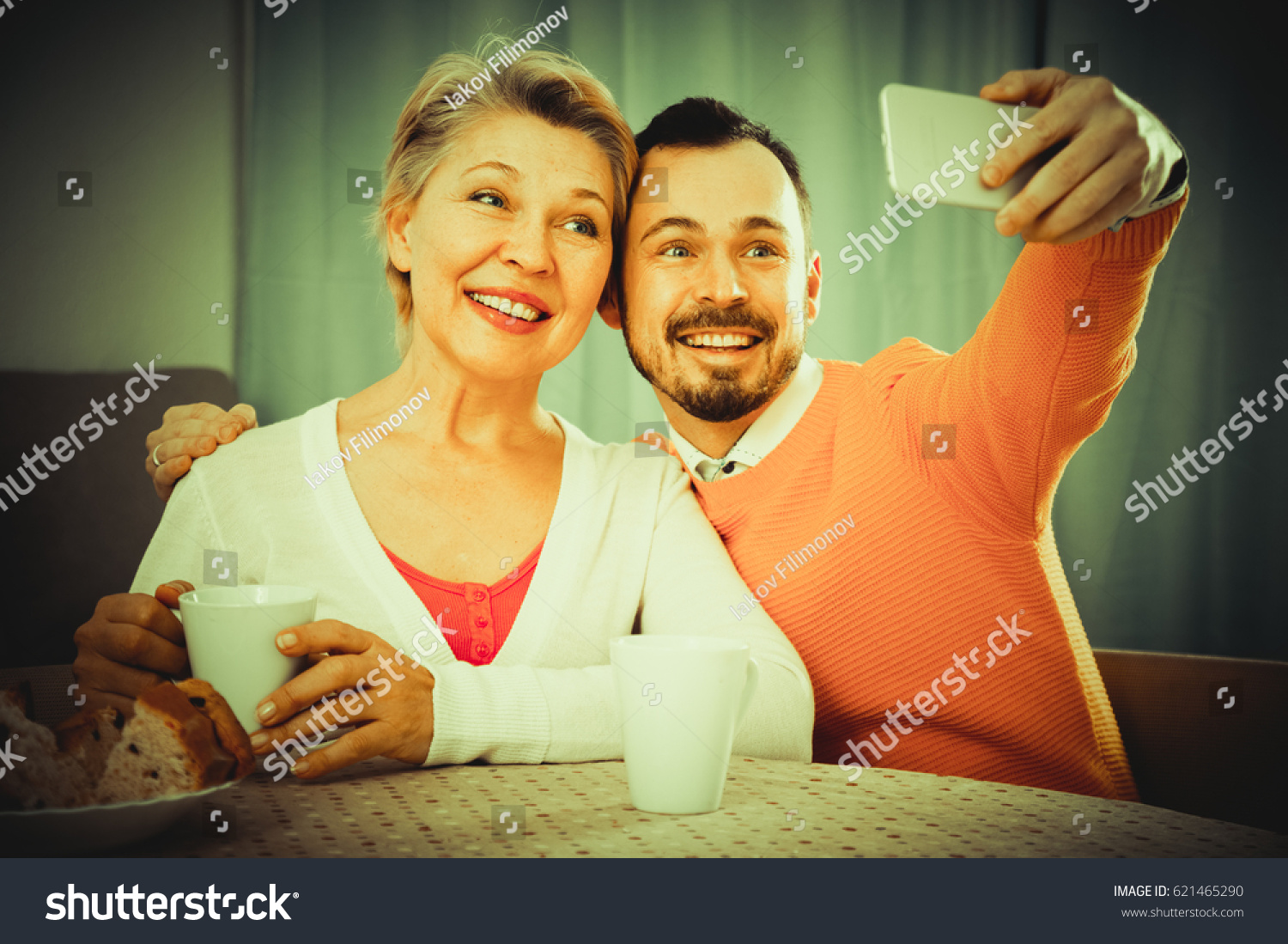 Smiling mother and adult son photographing together at home #621465290