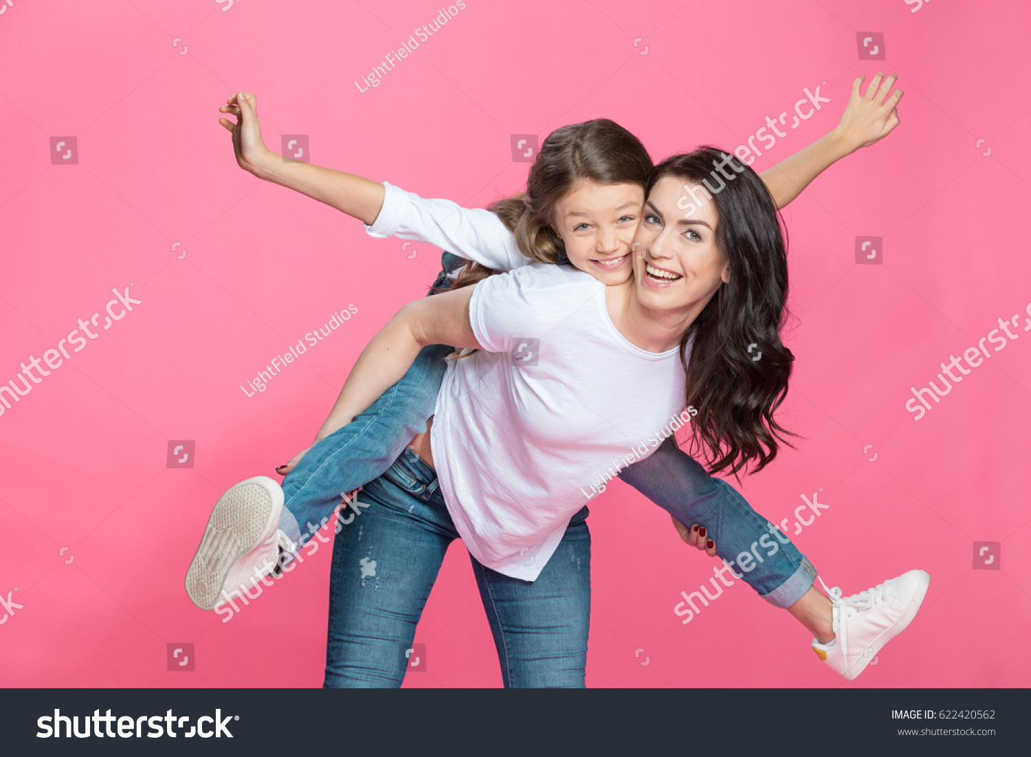 Happy mother piggybacking adorable little daughter smiling at camera #622420562