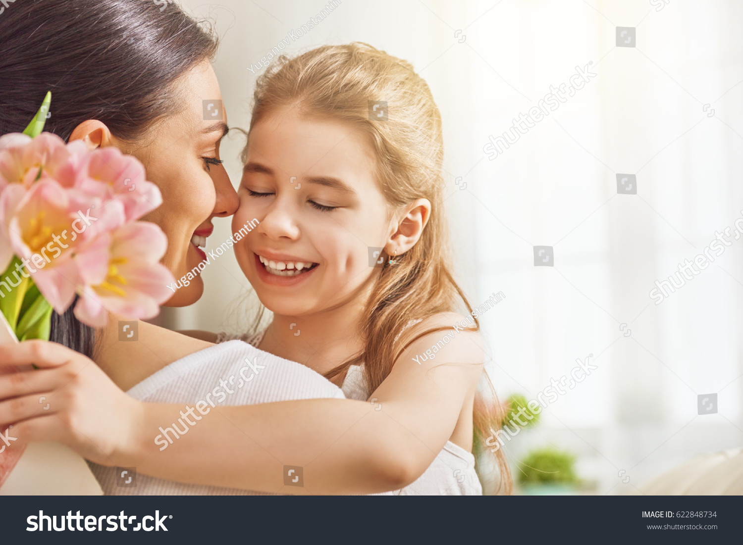 Happy mother's day! Child daughter congratulates mom and gives her flowers tulips. Mum and girl smiling and hugging. Family holiday and togetherness. #622848734