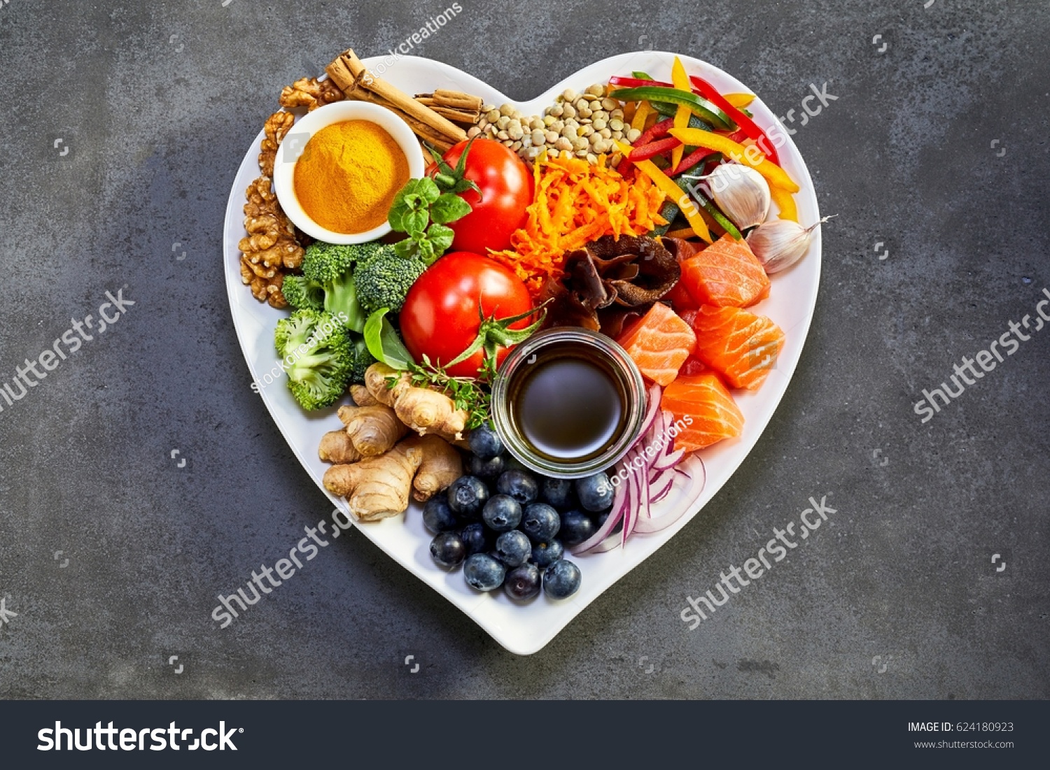 Healthy diet for the cardiovascular system with a heart-shaped plate of acai, lentils, soy sauce, ginger, salmon, carrot, tomato, turmeric, cinnamon, walnuts, garlic, peppers, broccoli, basil, onion #624180923