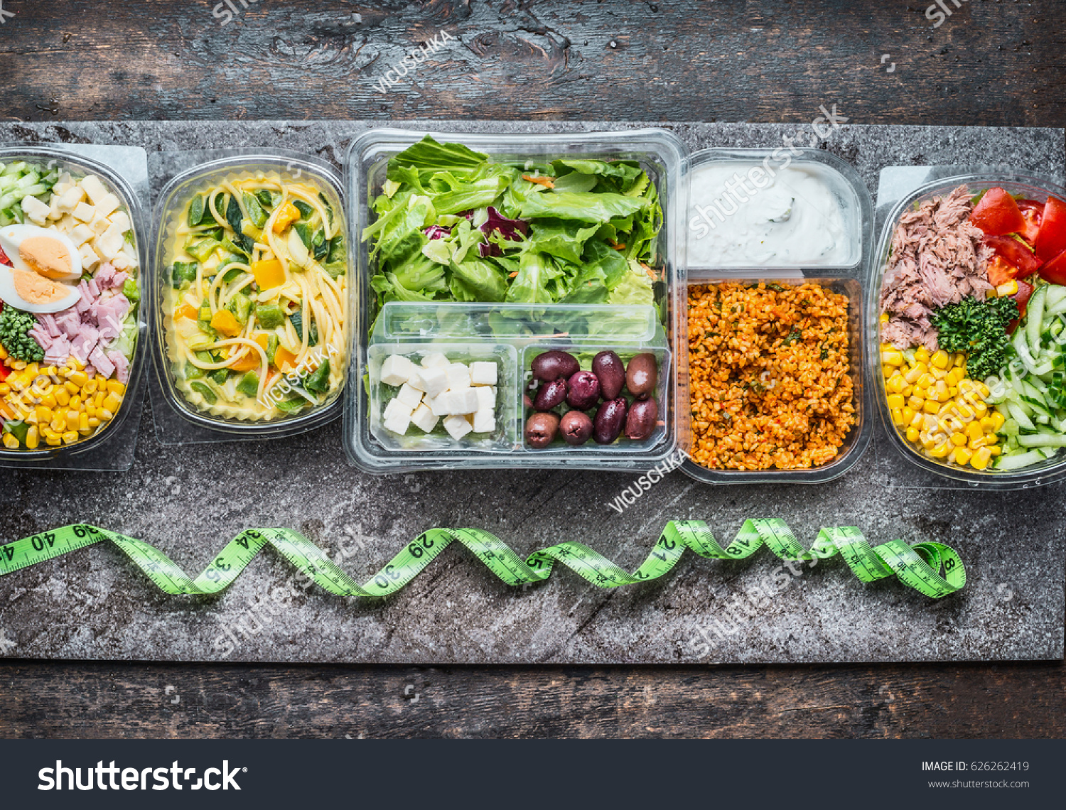 Various Healthy lunch boxes in  plastic package and green measuring tape on rustic background, top view. Dieting food concept. #626262419