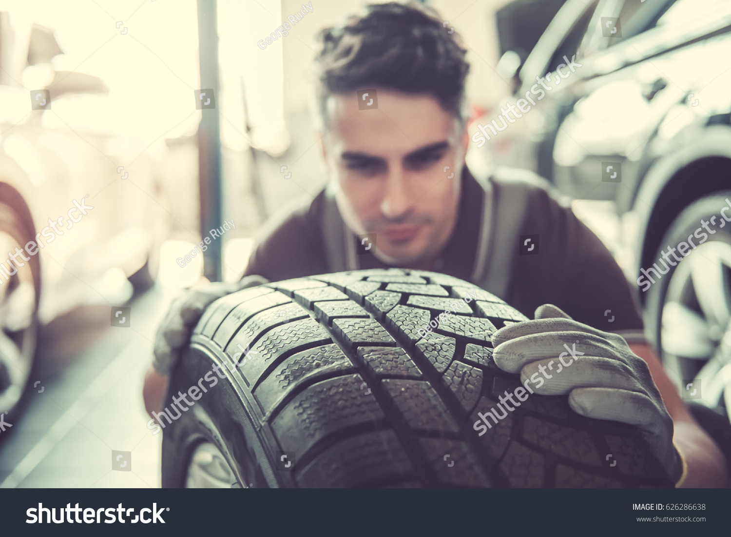 Handsome young auto mechanic in uniform is examining a tire while working in auto service #626286638