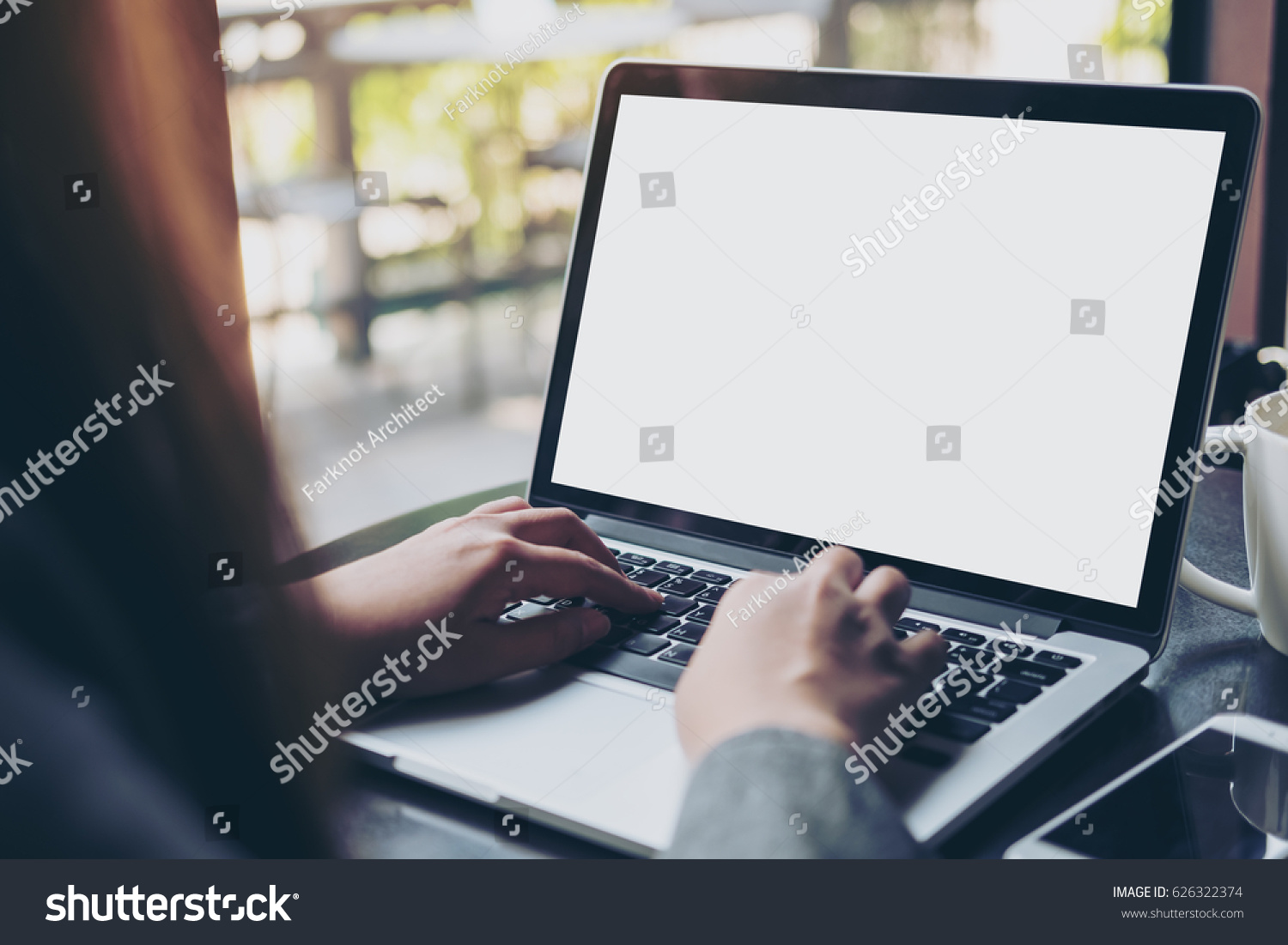 Mockup image of business woman using and typing on laptop with blank white screen and coffee cup on glass table in modern loft cafe #626322374