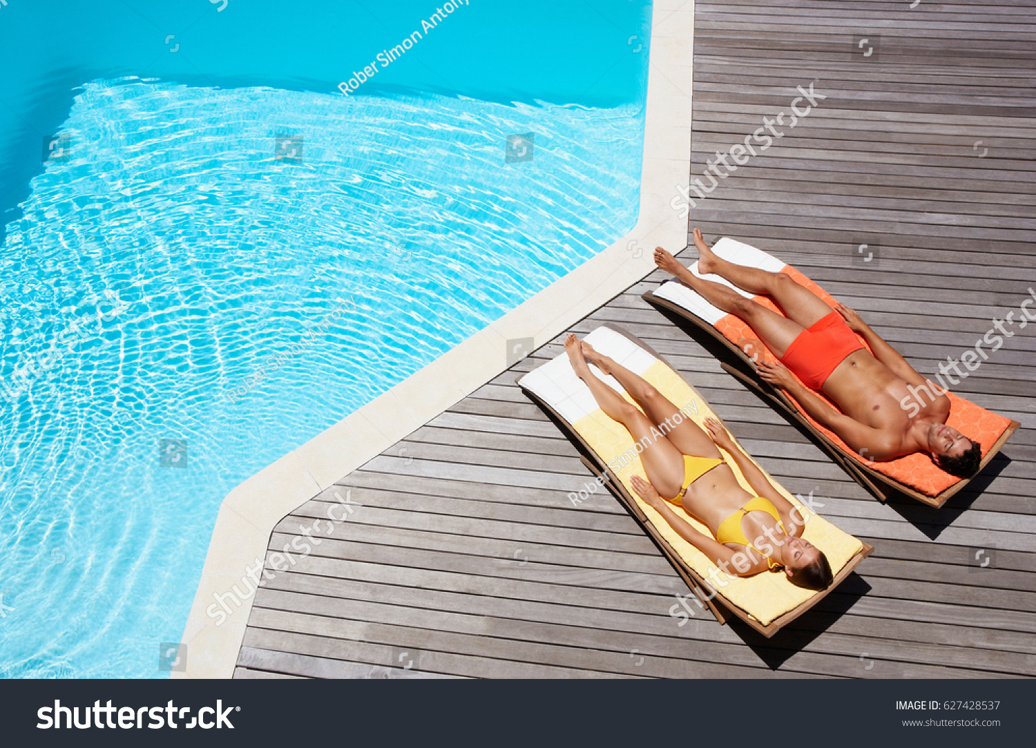 Full length of a young couple resting on sun loungers by swimming pool #627428537