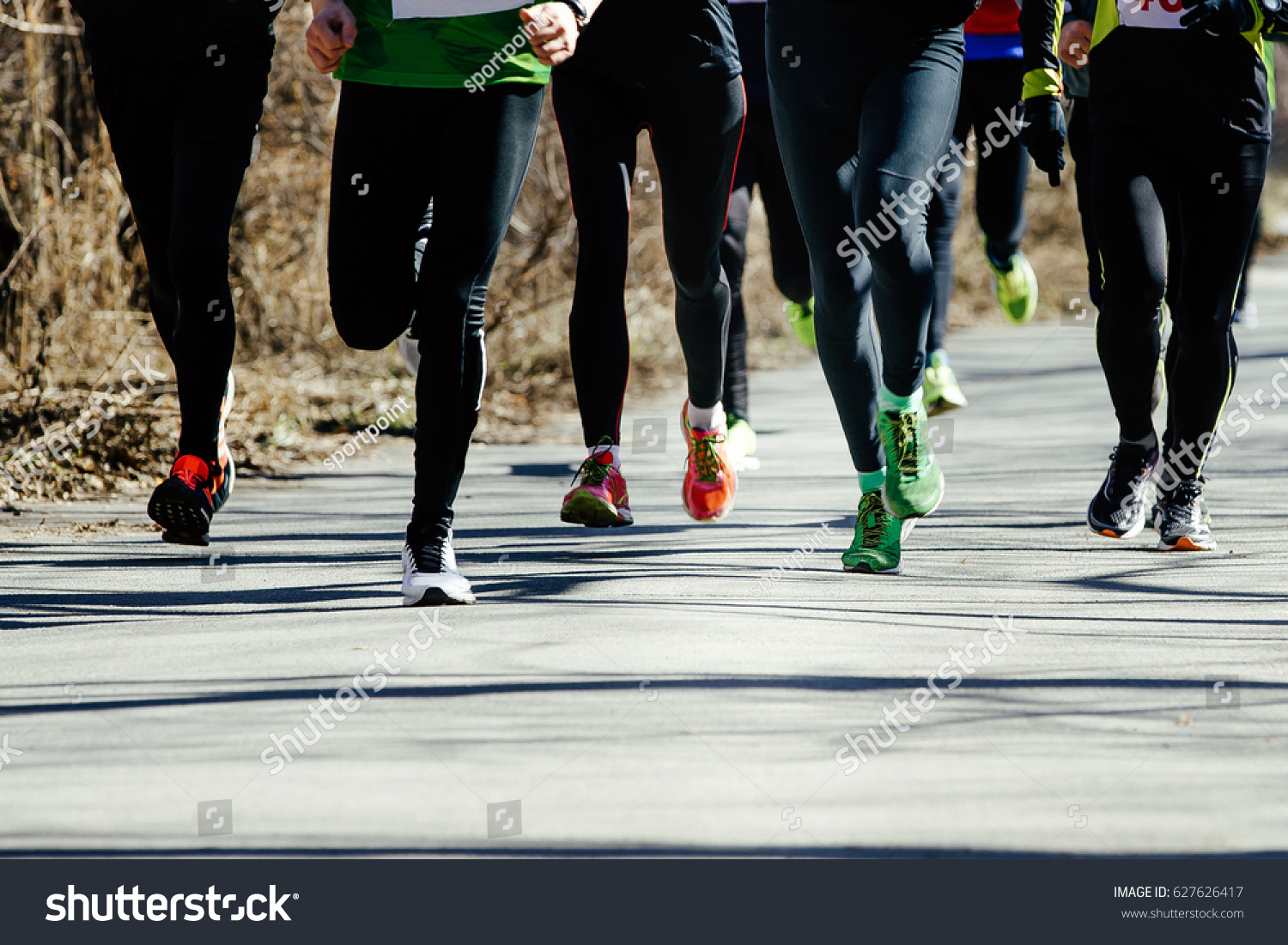 feet runners group leaders runnnig on asphalt road in a city park #627626417