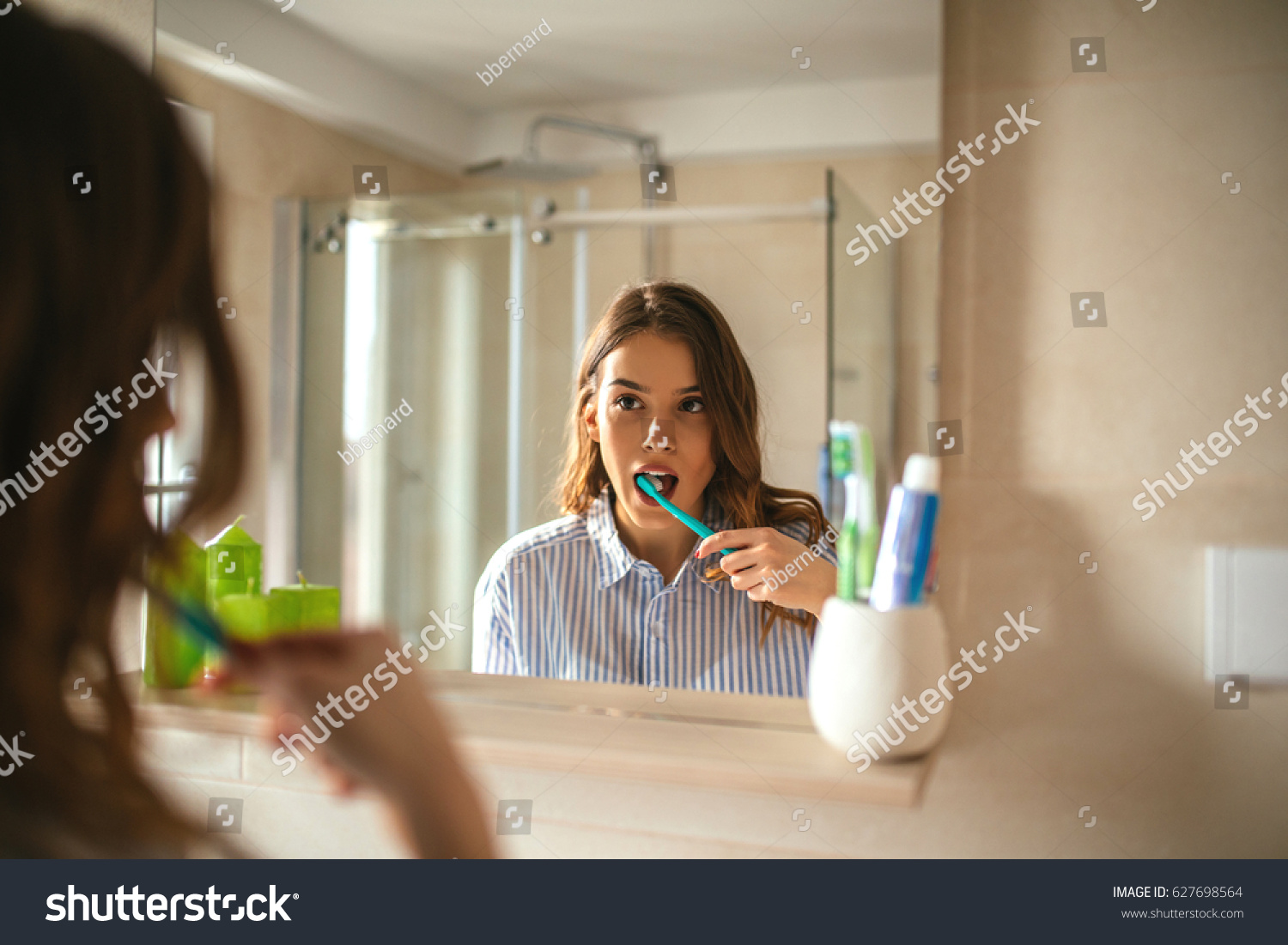 Portrait of a beautiful woman brushing teeth and looking in the mirror in the bathroom. #627698564