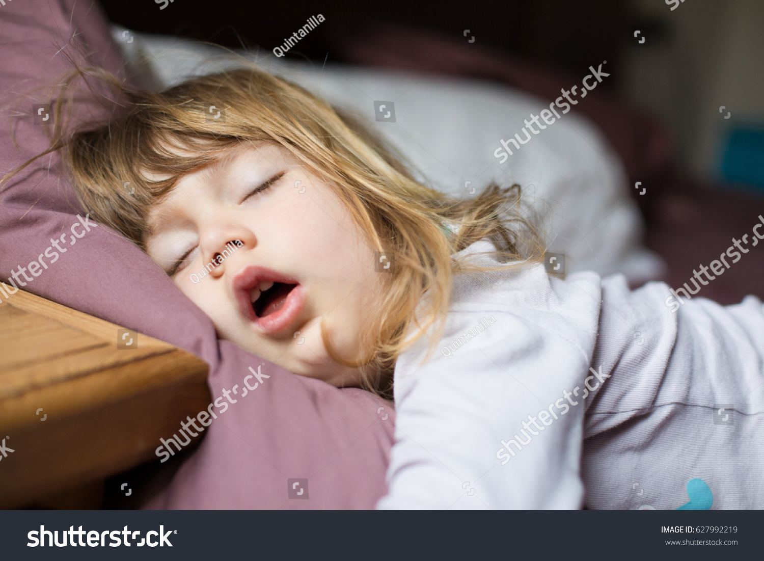 funny face expression with open mouth of blonde caucasian three years old child,  sleeping on  king bed #627992219