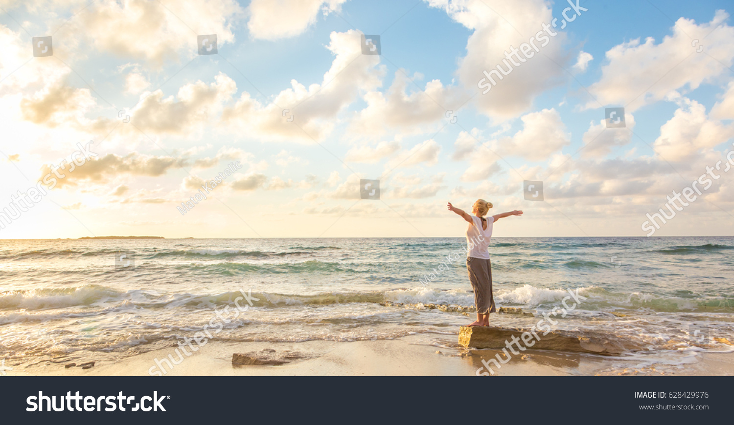 Relaxed woman enjoying sun, freedom and life an beautiful beach in sunset. Young lady feeling free, relaxed and happy. Concept of vacations, freedom, happiness, enjoyment and well being. #628429976