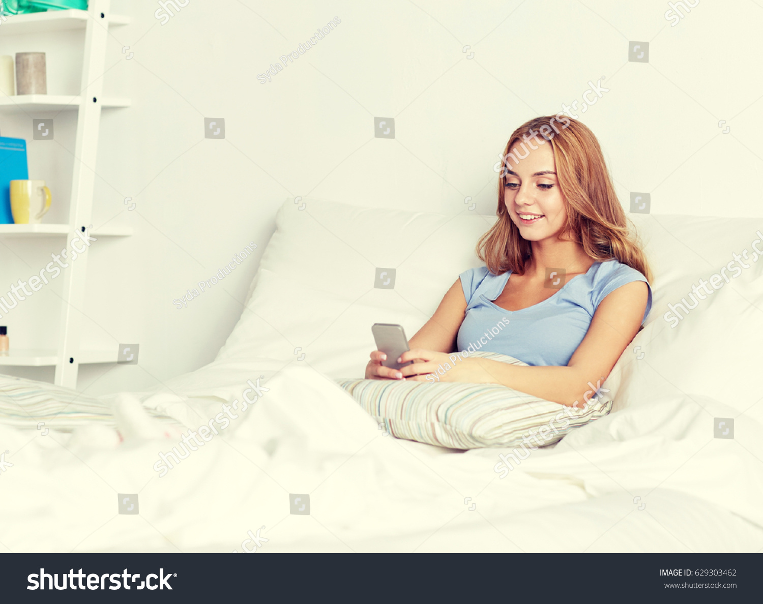 people, leisure and technology concept - happy woman or teenage girl with smartphone in bed at home #629303462