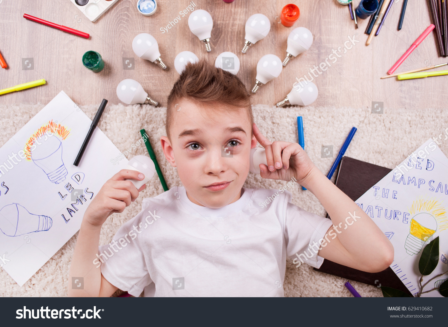 A little boy lies among the markers and drawings of LED bulbs #629410682