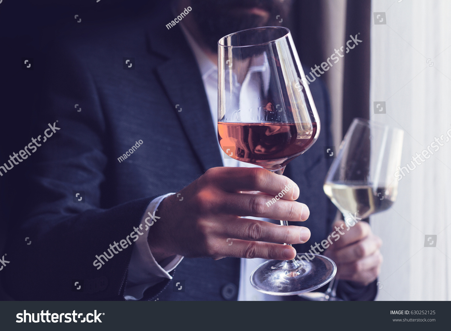 horizontal close up of a Caucasian man with beard black suit and white shirt offering a tall glass of rose wine at an event by the window natural light #630252125