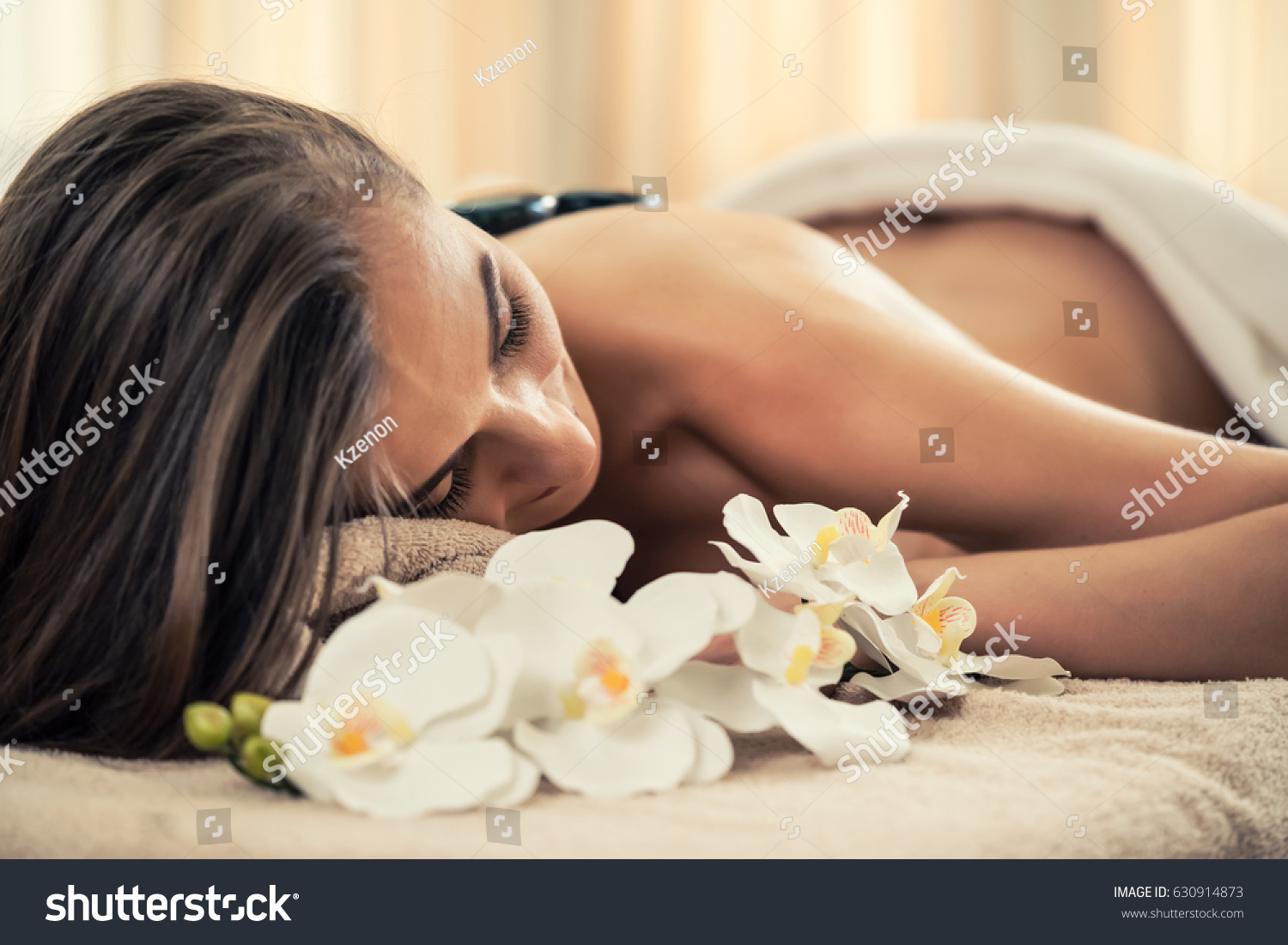 High angle view of young woman lying down on massage bed with traditional hot stones along the spine at spa and wellness center  #630914873
