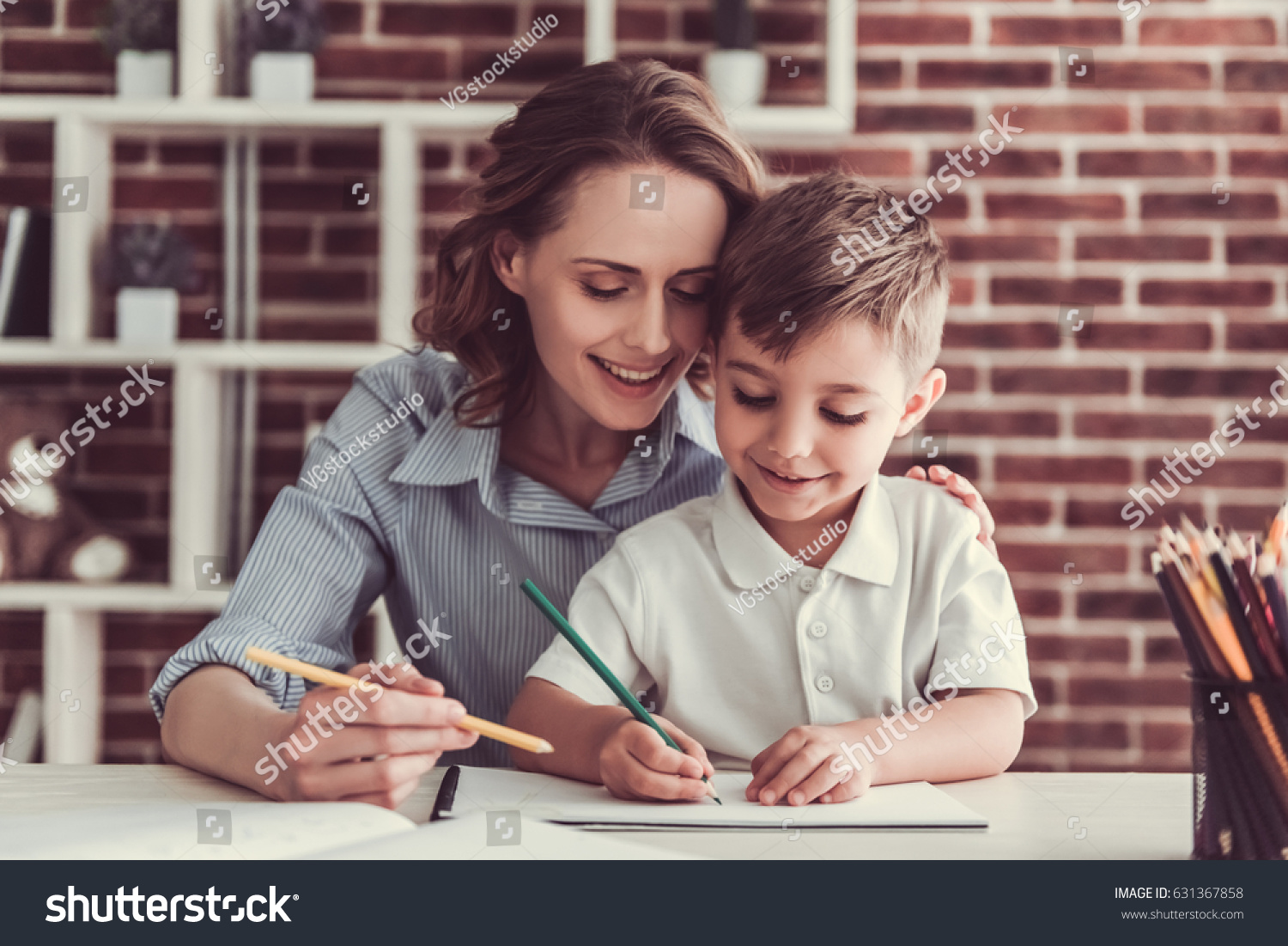 Beautiful business woman and her cute little son are drawing and smiling while sitting in office #631367858