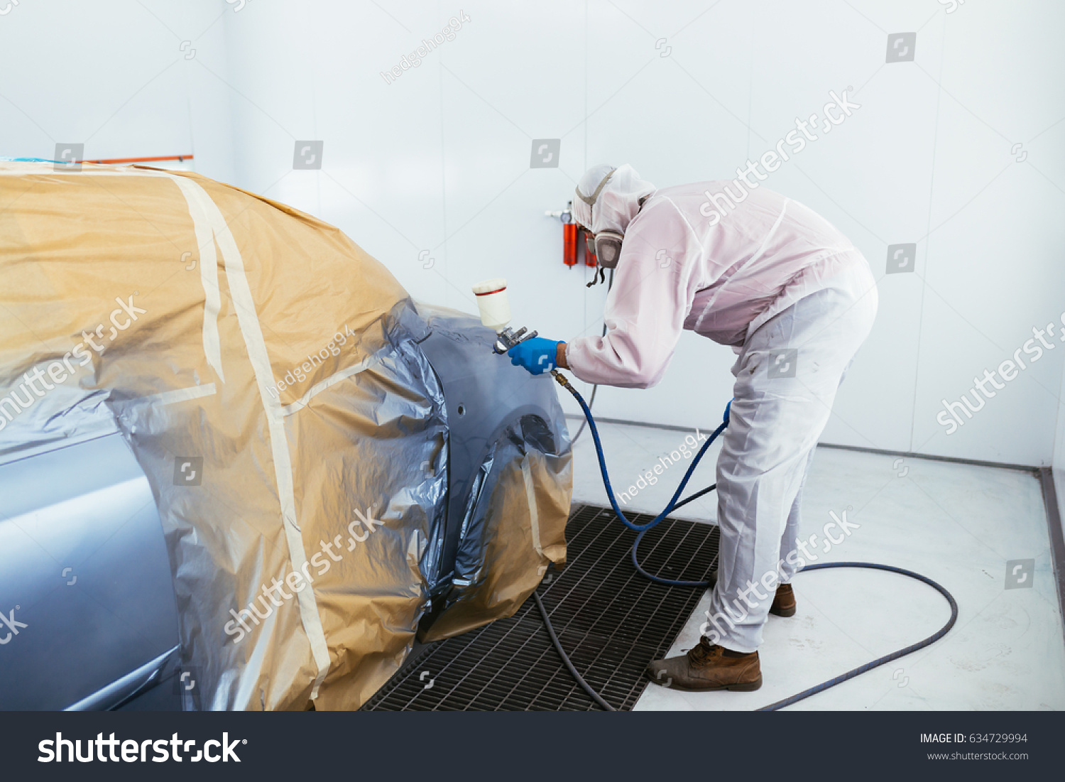 Man with protective clothes and mask painting car using spray compressor. Selective focus.  #634729994