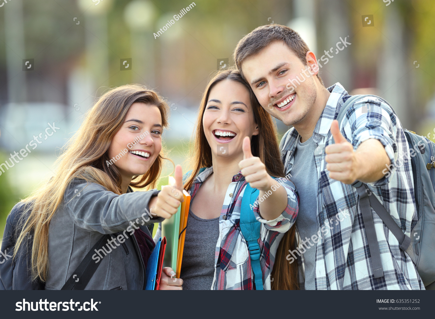 Three happy students looking at you with thumbs up in an university campus #635351252