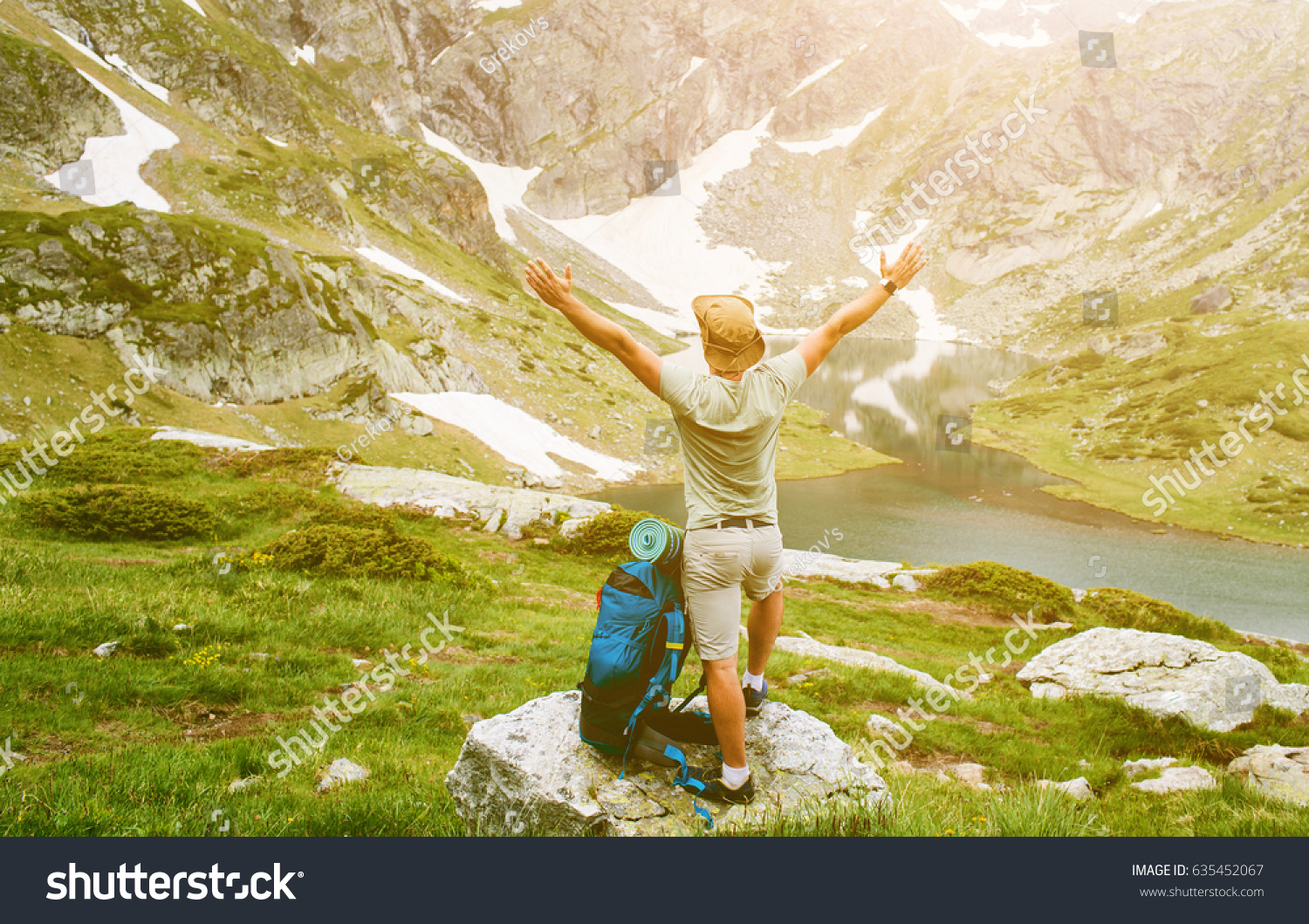 Young man with backpack standing with raised hands on the mountain and enjoying valley view #635452067
