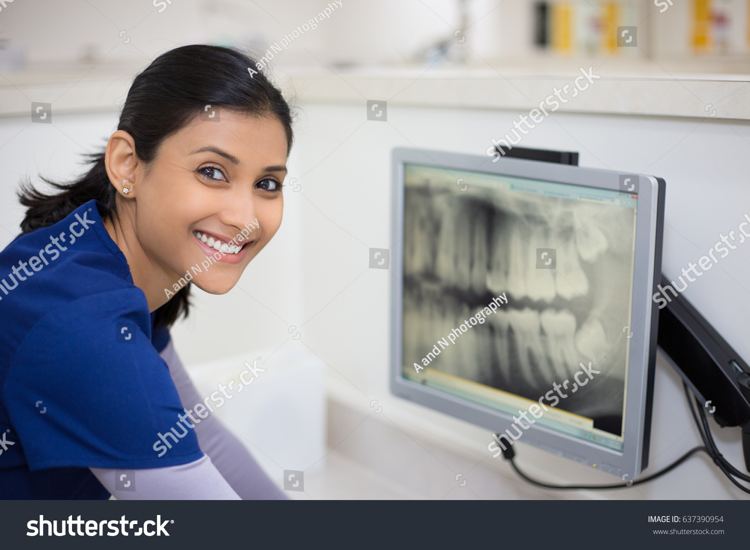 Closeup portrait of allied health dental professional in blue scrubs examining dental x-ray on computer screen, isolated dentist office #637390954