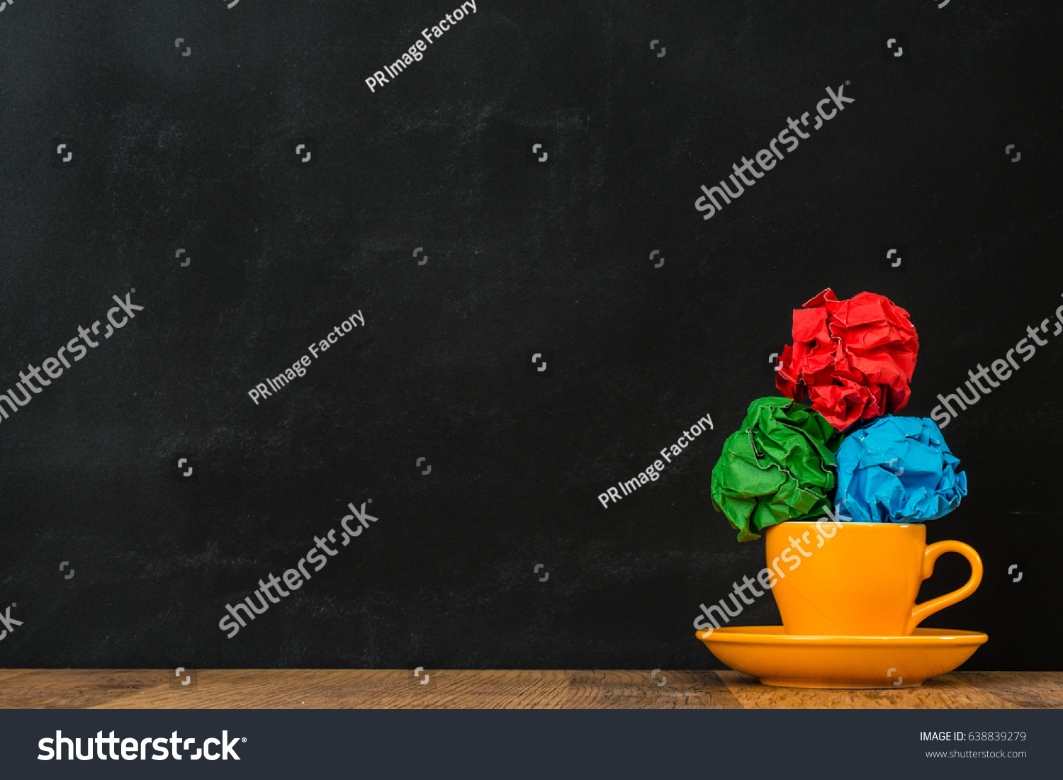 smooth glossy ceramic orange coffee cup put on the wooden surface table with color paper balls stacked together showing blackboard background. #638839279