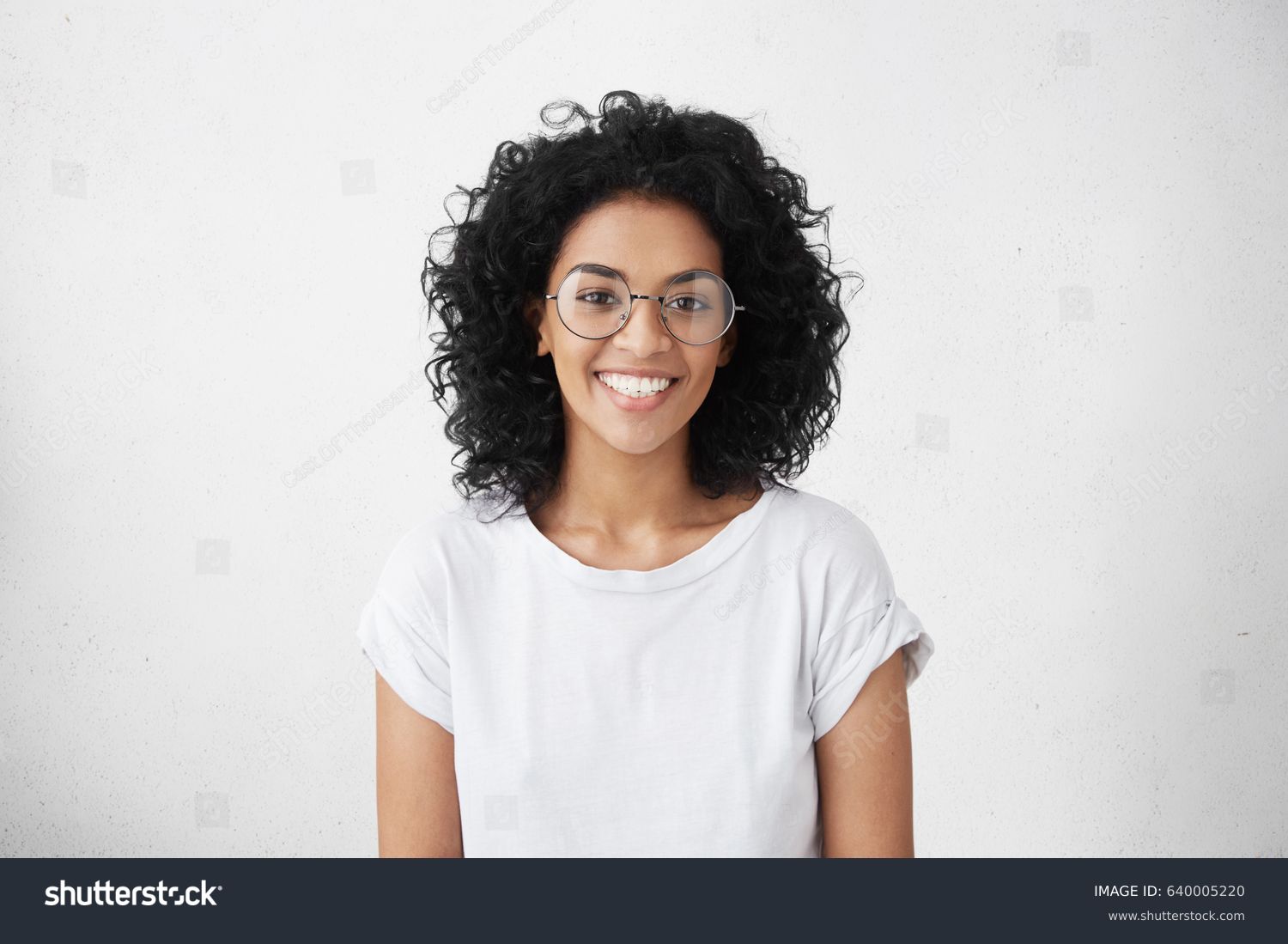 Indoor portrait of beautiful brunette young dark-skinned woman with shaggy hairstyle smiling cheerfully, showing her white teeth to camera while feeling happy and carefree on her first day-off
