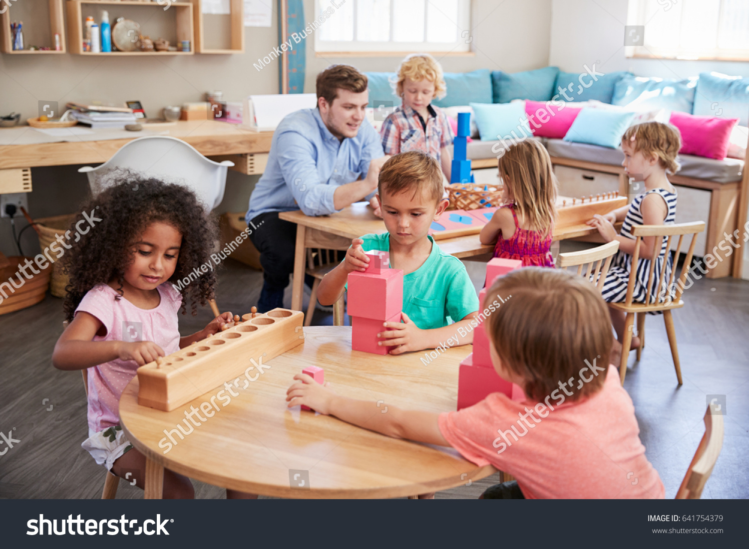 Teacher And Pupils Working At Tables In Montessori School #641754379