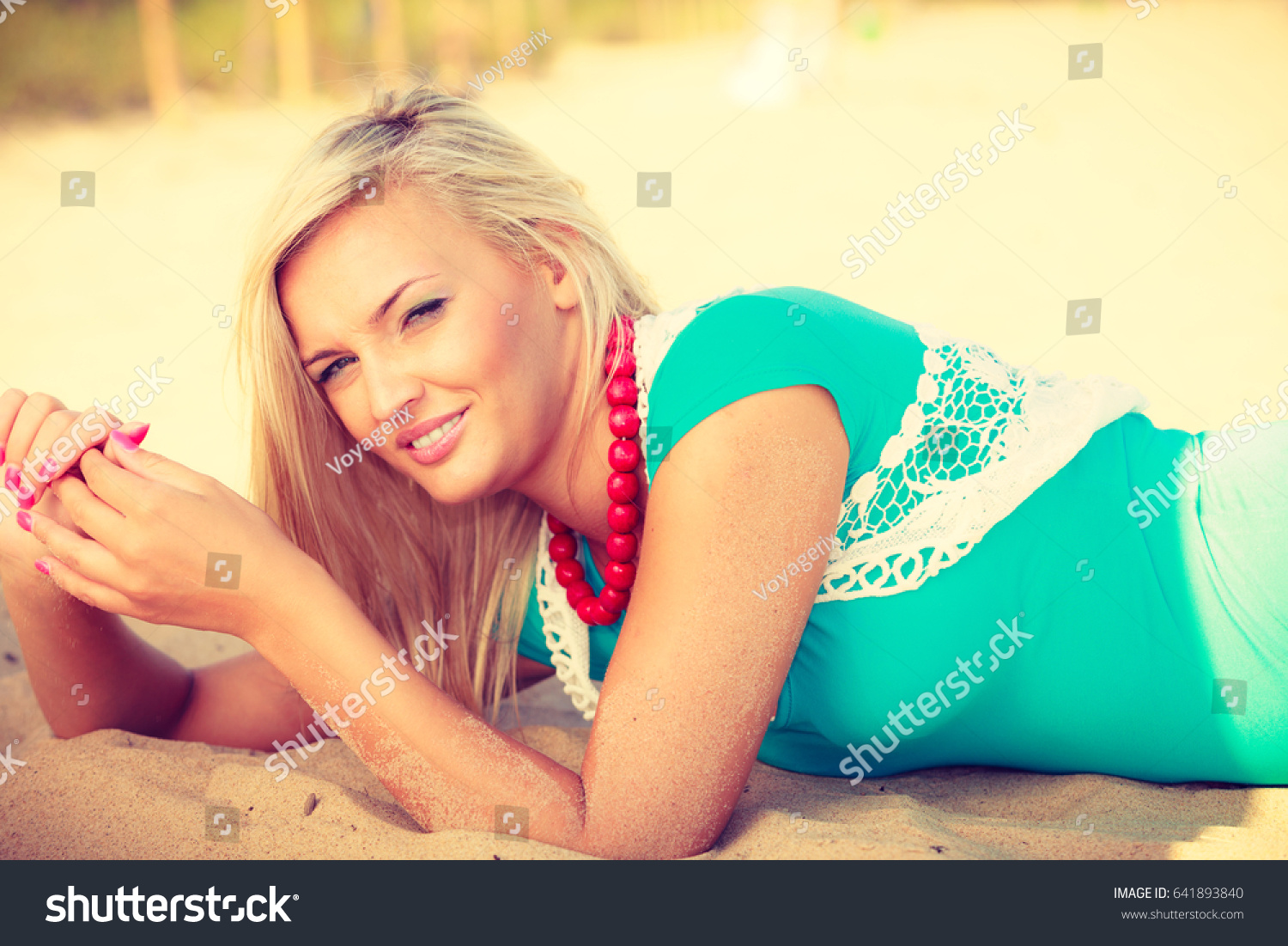 Portrait of attractive blonde woman lying on sandy beach relaxing during summertime #641893840