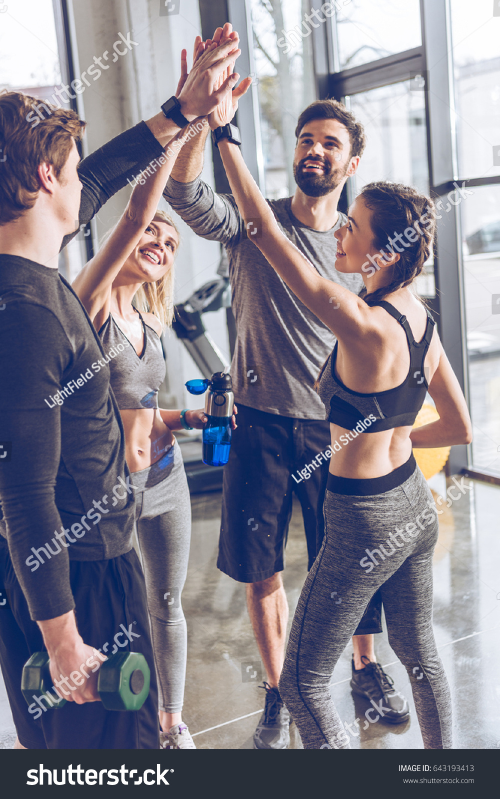 Happy young athletic people in sportswear giving high five in gym #643193413