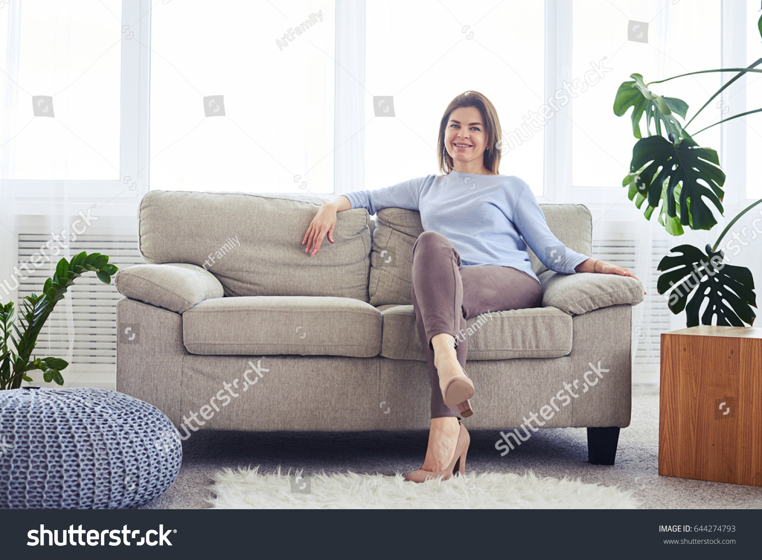 Wide shot of woman in fashionable clothes sitting on sofa in bright living room #644274793