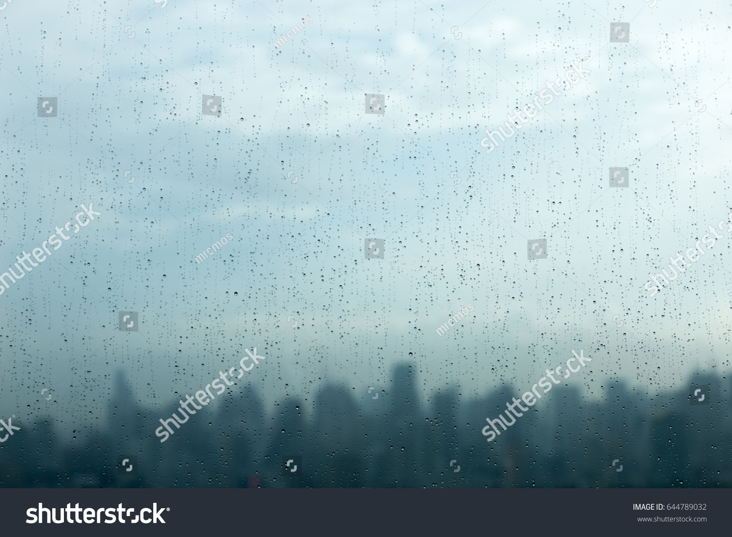 Rain drops on window glass and blurred cityscape and sunlight in background. #644789032